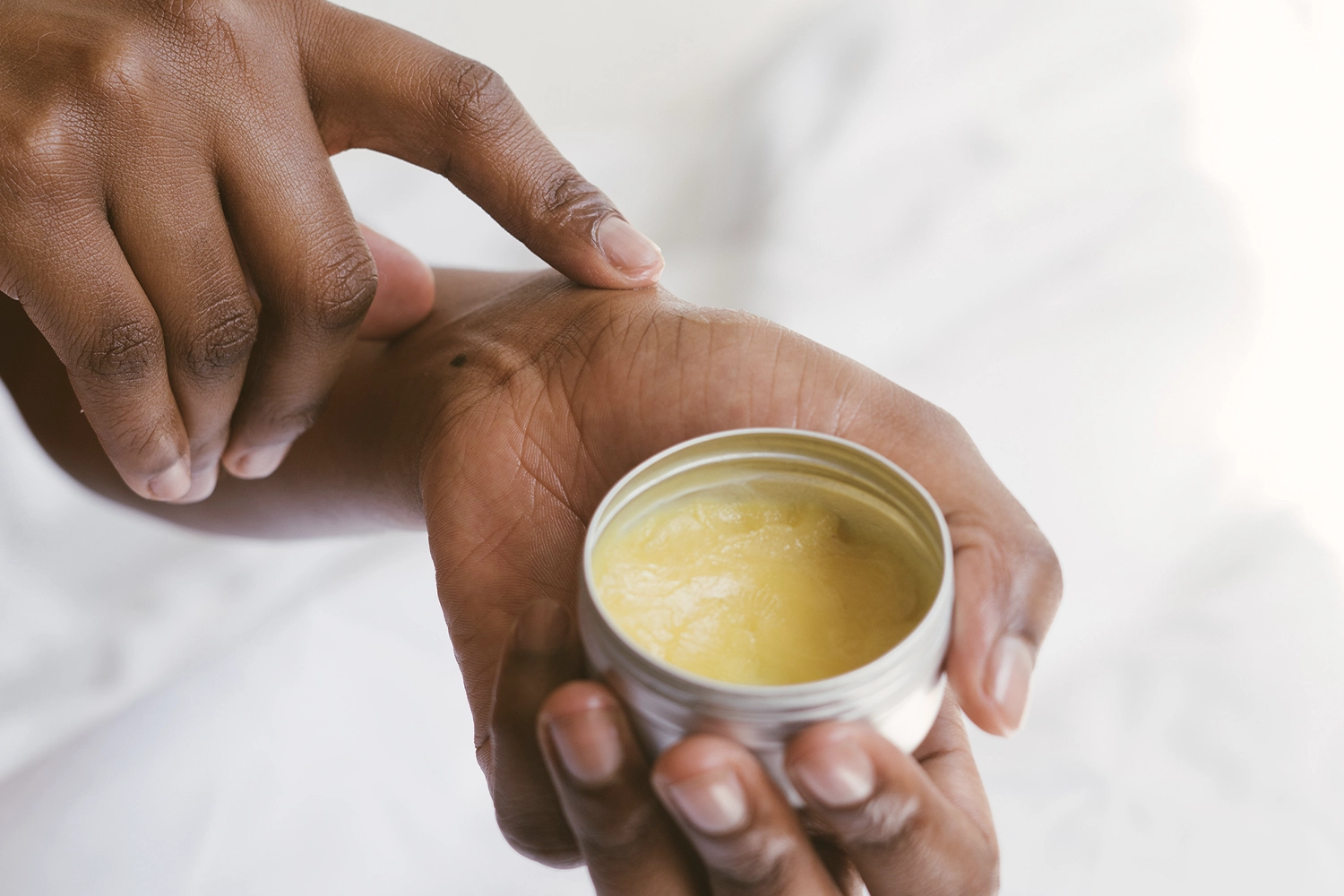 hand holding tub of ointment and applying to skin